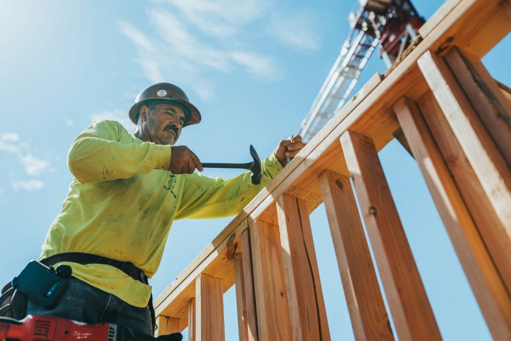Construction workers assembling wood framing against a bright sky